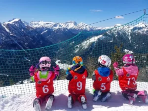 Dzieci w strojach narciarskich patrzące na ośnieżone góry we Włoszech.