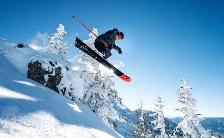 Mężczyzna skaczący na nartach na tle ośnieżonych choinek.